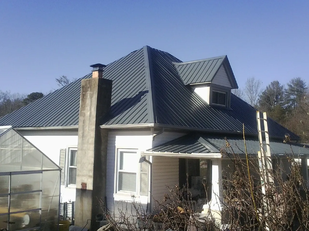 Dark blue standing seam metal roof on a white farmhouse with dormer — Slate & Tile Roof Repair by Roofing Brothers in North Myrtle Beach