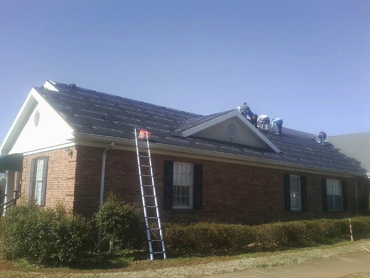 Crew tearing shingles off a brick ranch roof with a ladder set — Emergency Roof Repair work by our crew in North Myrtle Beach