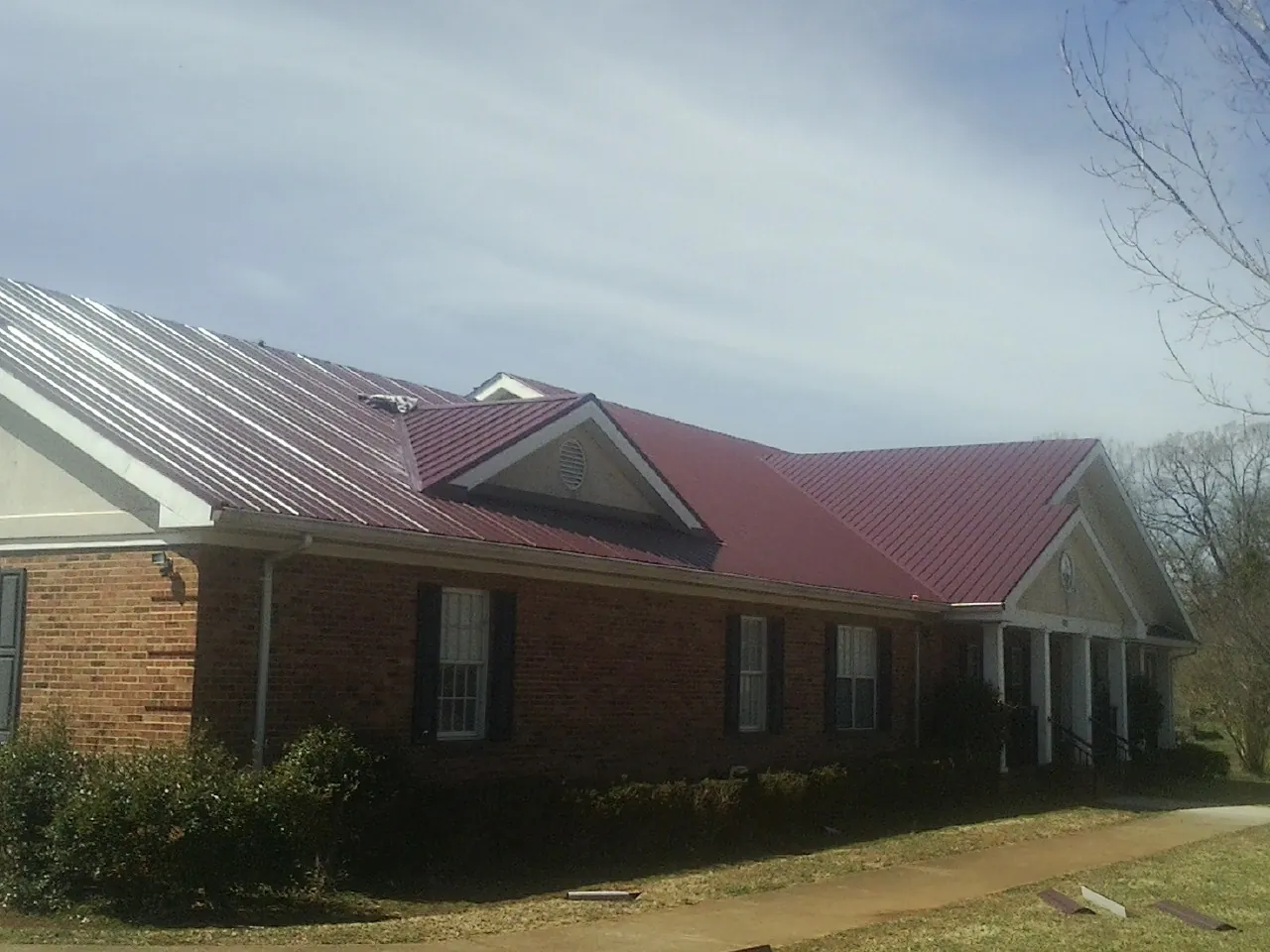Red metal roof with gabled entries on a long brick building, from a Hail Damage Roof Repair job in North Myrtle Beach