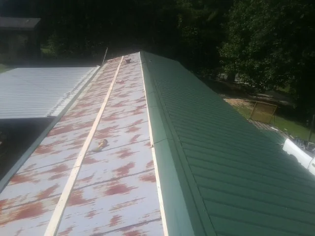 Old rusted panels beside newly installed green metal roofing — Wind Damage Roof Repair by Roofing Brothers in North Myrtle Beach