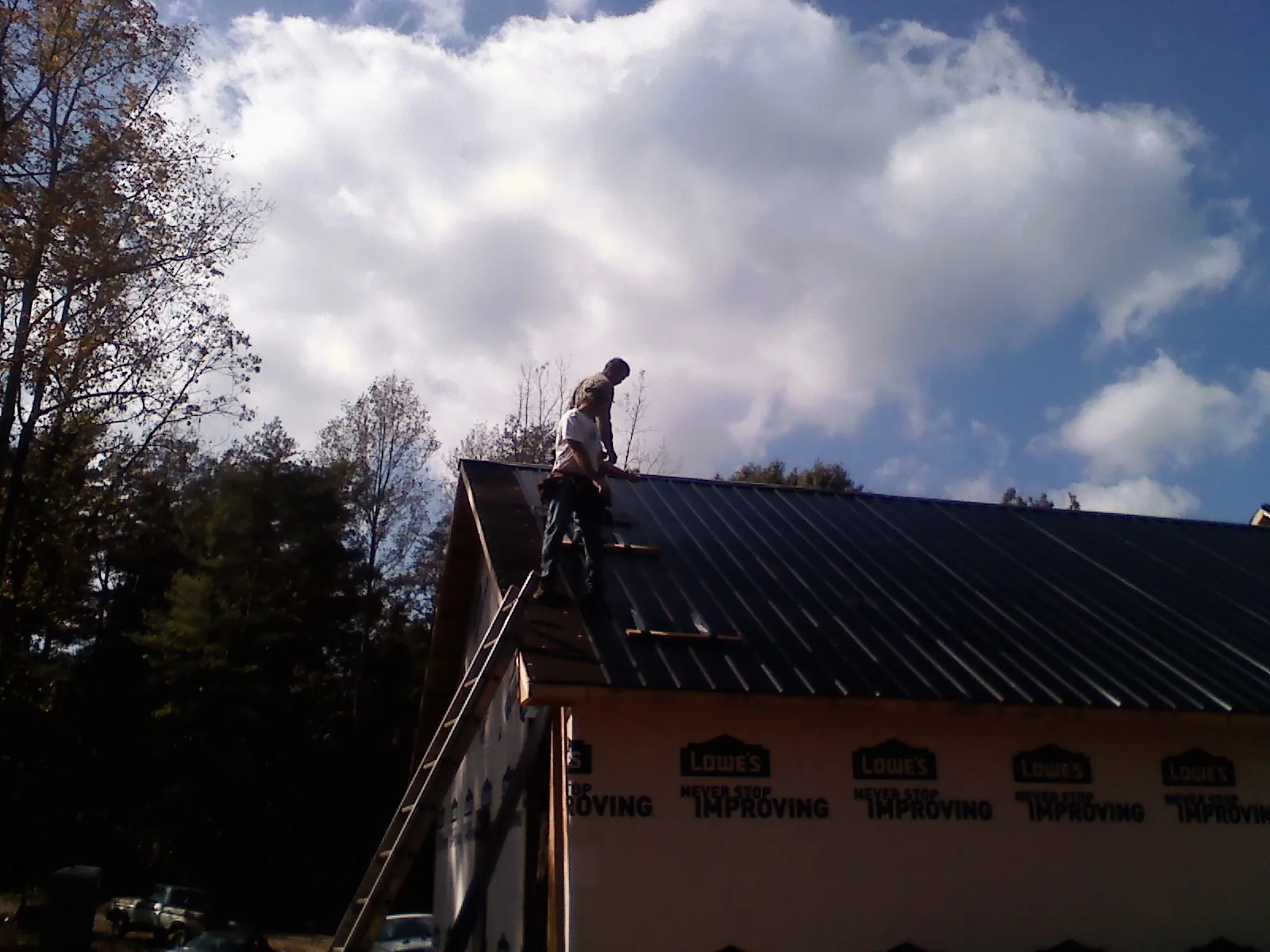 Roofer fastening dark metal panels high against a cloudy sky, from a Roof Inspection job in North Myrtle Beach