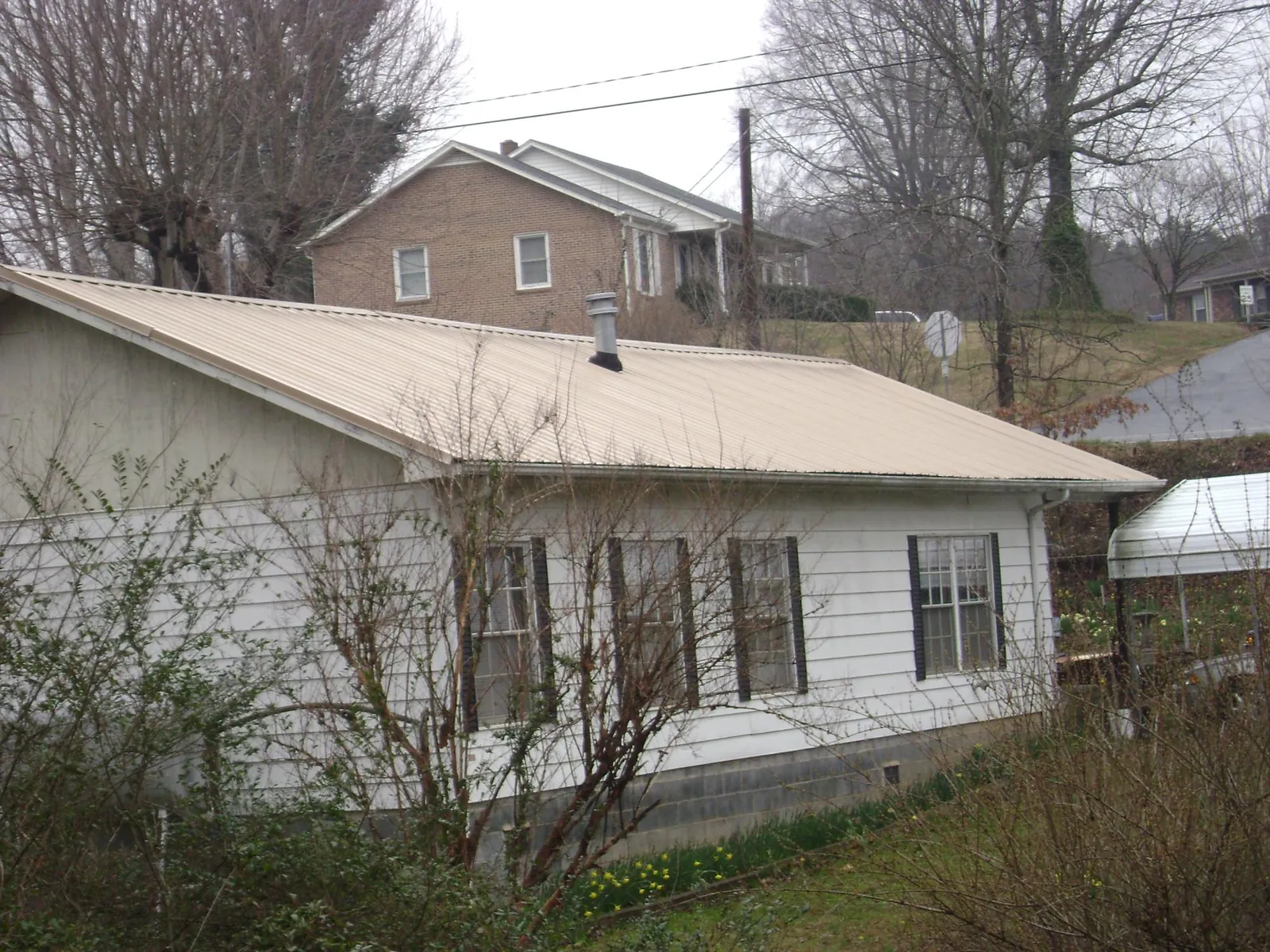 Tan metal roof on a white sided house set into a hillside — Commercial Roofing by Roofing Brothers in North Myrtle Beach
